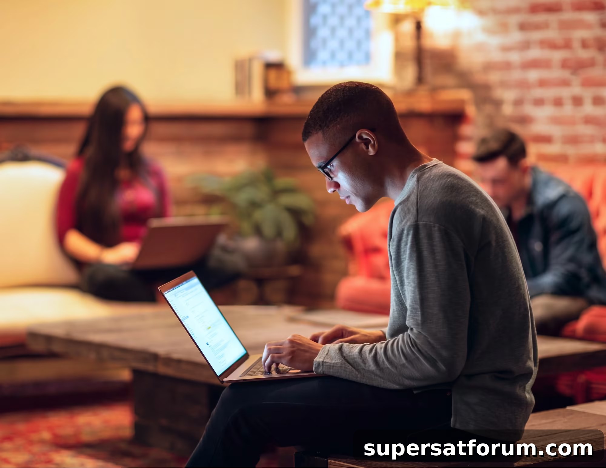 Qyx Qj Hero X | IT-Branschen Person using a laptop indoors with others engaged in various activities in the background.